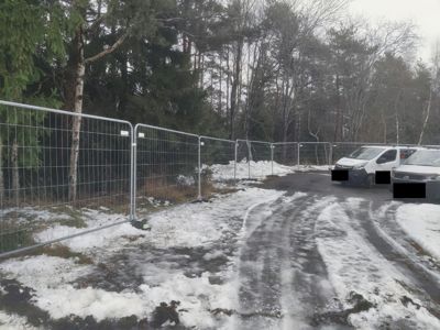 Fotografi av et bygge- eller anleggsområde med midlertidig hekk, snø på bakken og parkerte biler.
