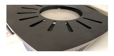 Fotografi av en svart, perforert overflate med et sentralt hull, sannsynligvis en del av en bygning eller innredning.