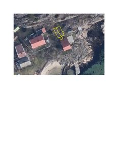 Luftfoto (satellittbilde) av et kystområde med flere hus og en markert tomt i gult.