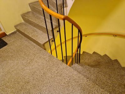 Fotografi av en spiraltrapp med trinn i betong, svart stangverk og en buet håndtak i tre.