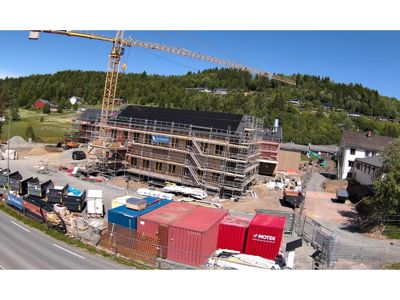 Fotografi av en byggeplass med et hus under oppføring, omgitt av kran, stålrammer, containere og utstyr.