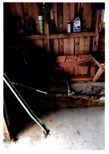 Fotografi av en innendørs situasjon, sannsynligvis i en garasje eller underetasje, som viser en betongfundament, en trekonstruksjon og diverse gjenstander.