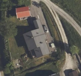 Luftfoto (satellittbilde) av en tomt med en hovedbygning, en mindre bygning og omgivende natur.