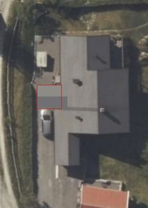 Luftfoto (flyfoto) av en bygning sett fra oven, med omgivende tomt og vei.