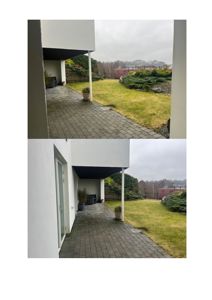 Fotografi av en moderne bygning sett fra utsiden, som viser en terrasse med flislagt gulv, en hvit fasade, en dør og en hage med gress og busker.