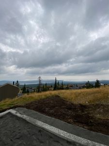 Fotografi av et byggefelt med en nybetongert grunnplatt i forgrunnen, en grå himmel og nabolag i bakgrunnen.