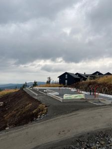 Fotografi av en byggeplass som viser fundamentarbeider i gang, med ferdige hus i bakgrunnen.