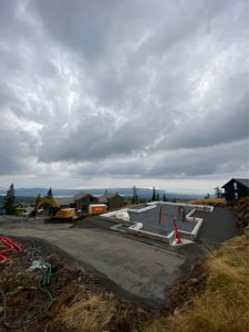 Fotografi av en byggeplass med fundamentarbeider i gang, inkludert graving, betongfundament og en gullgraver.