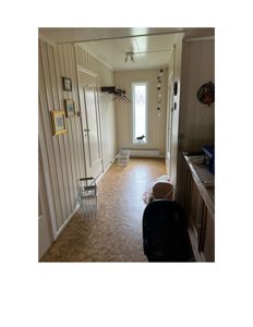 Fotografi av en gang eller korridor inne i en bolig, med synlige dører, vindu, gulv og innredning.