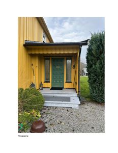 Fotografi av en gul bygning med grønn dør og en tilbygggang.