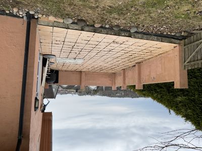 Fotografi av en terrasse med tak, sett fra siden. Bildet viser fasaden, takkonstruksjonen og omgivelsene.