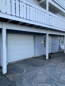 Fotografi av fasaden på en bygning med garasje, inngangsdør og balkong.