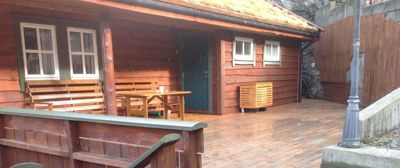 Fotografi av en liten, trepanelt hytte med et grønt tak, en veranda med møbler og en trapp opp til en terrasse.