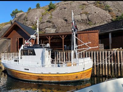 Fotografi av en båt som er fortøyd ved en kai med trebygninger i bakgrunnen.