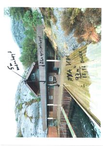 Fotografi av en eksisterende bygning (tømmerhytte) på en klippeside med vann i forgrunnen. Bildet har håndskrevne notater om mål og areal.