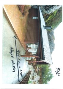 Fotografi av en eksisterende hytte sett fra siden, med håndskrevne mål og dato på bildet.