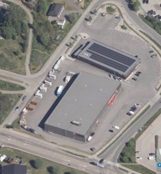 Luftfoto av to bygninger på en tomt med parkeringsplasser og veier.