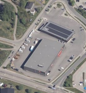 Luftfoto av to bygninger på en tomt med parkeringsplasser og veier.