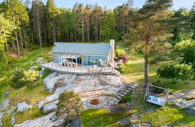 Fotografi av en moderne hytte sett fra luften, plassert på en steinete bakke i skogen.