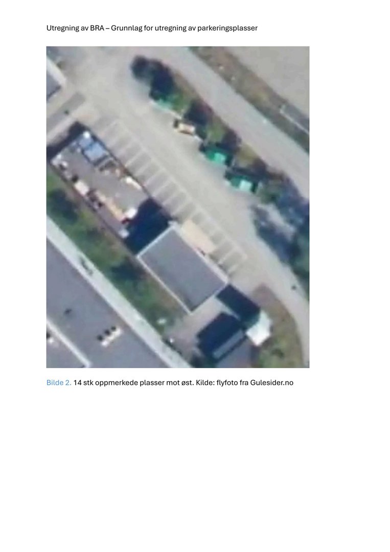 Flyfoto av et område med parkeringsplasser og bygninger.