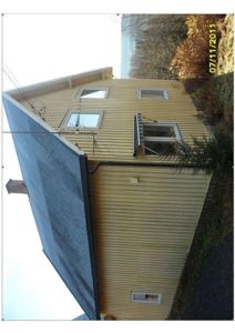 Fotografi av en gul, trepanelt bygning sett fra siden. Bildet viser fasaden, vinduer, tak og en del av omgivelsene.