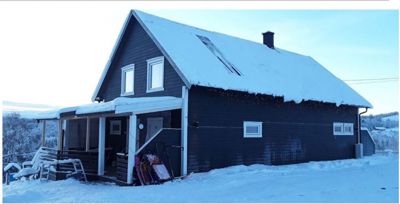 Fotografi av en mørk hytte med snø på taket og i omgivelsene.