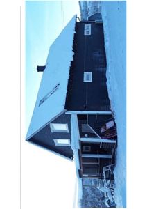 Fotografi av en mørk, toetters hus med snø på taket og i omgivelsene.