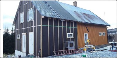 Fotografi av en bygning under oppføring eller renovering, med synlig takarbeid og utstyr på plassen.