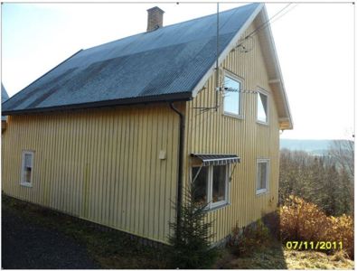 Fotografi av en gul, toetasjes hytte med skifer- eller blikkdekket tak, sett fra siden.