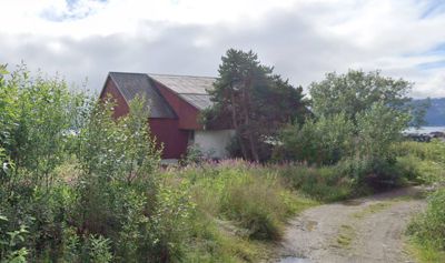 Fotografi av en rød bygning (barn) sett fra utsiden, omgitt av vegetasjon og med en sti i forgrunnen.