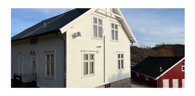 Fotografi av en hvit, toetasjes bygning med svart tak sett fra siden og foran.