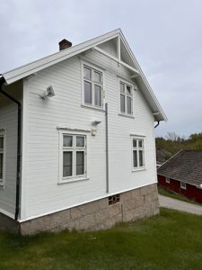 Fotografi av en hvit, toetasjes villa sett fra siden. Bildet viser fasaden, vinduene, taket, nedløp og fundamentet.