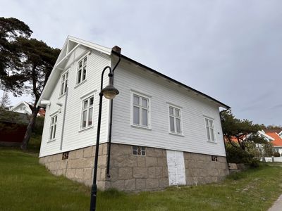 Fotografi av en hvit, toetasjes bygning med steinfundament sett fra siden.