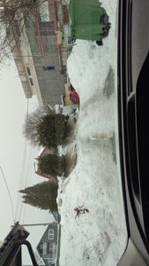 Fotografi tatt fra bil som viser en snødekt vei, nabolagshus og en bygning under oppføring i bakgrunnen.