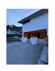 Fotografi av en moderne bygning sett fra utsiden, med fokus på fasaden, en åpen garasje og en steinmur i forgrunnen.