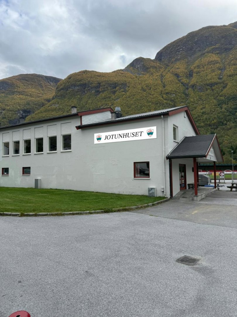 Fotografi av et hvitt bygg med skiltet 'JOTUNHUSET' foran en fjellbakke.