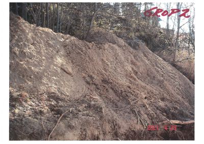Fotografi av en jordhaug eller utgravd terrengform med skog i bakgrunnen.