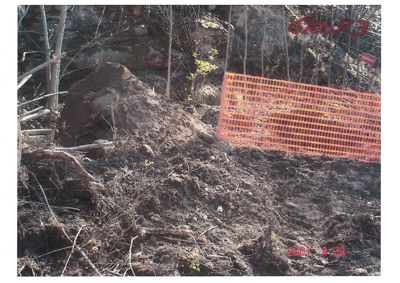 Fotografi av et bygge- eller grunngjennomføringsområde med oppgravd jord og en oransje sikkerhetshekk.