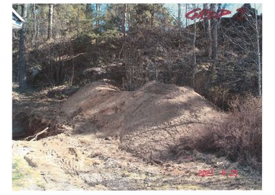 Fotografi av et utgravet område med jordhøyer og skog i bakgrunnen.