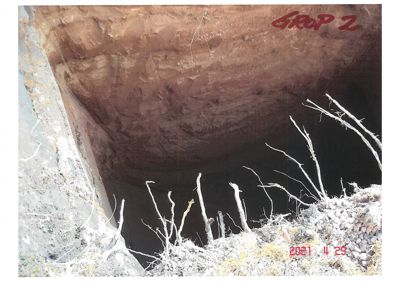 Fotografi av en utgravd grop eller grøft på byggeplass, med jordvegger og rester av vegetasjon.