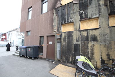 Fotografi av en bygning som ser ut til å være under renovering eller reparasjon, med en del av fasaden dekket av svart materiale og vinduer tettet med sperrplater.