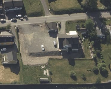 Luftfoto av en tomt og nabolag med hus, veier og parkeringsplasser.