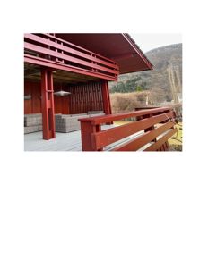 Fotografi av en uteplass med rød trekonstruksjon, møbler og utsikt over fjell.