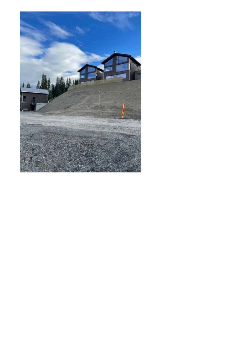 Fotografi av to moderne hus på en skråning under en blå himmel med skyer. Bildet viser også en grusvei i forgrunnen og en mindre bygning til venstre.