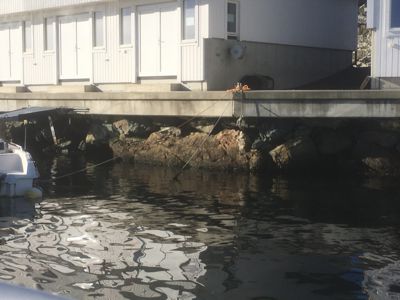 Fotografi av en bygning sett fra vannet, som viser fasaden og fundamentet på stein.