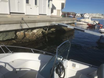 Fotografi av en brygge med hvite båthytter, en nedslått løftbrygge og flere båter i vannet.