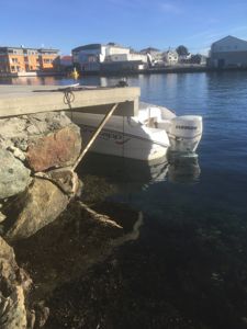 Fotografi av en båt ved kai med bygninger i bakgrunnen.