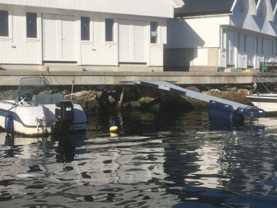 Fotografi av en brygge med båter og et hvitt hus i bakgrunnen.