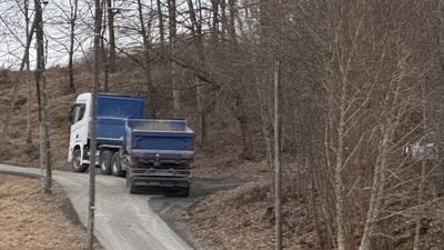 Fotografi av en blå og hvit lastebil som kjører på en vei gjennom et skogområde.