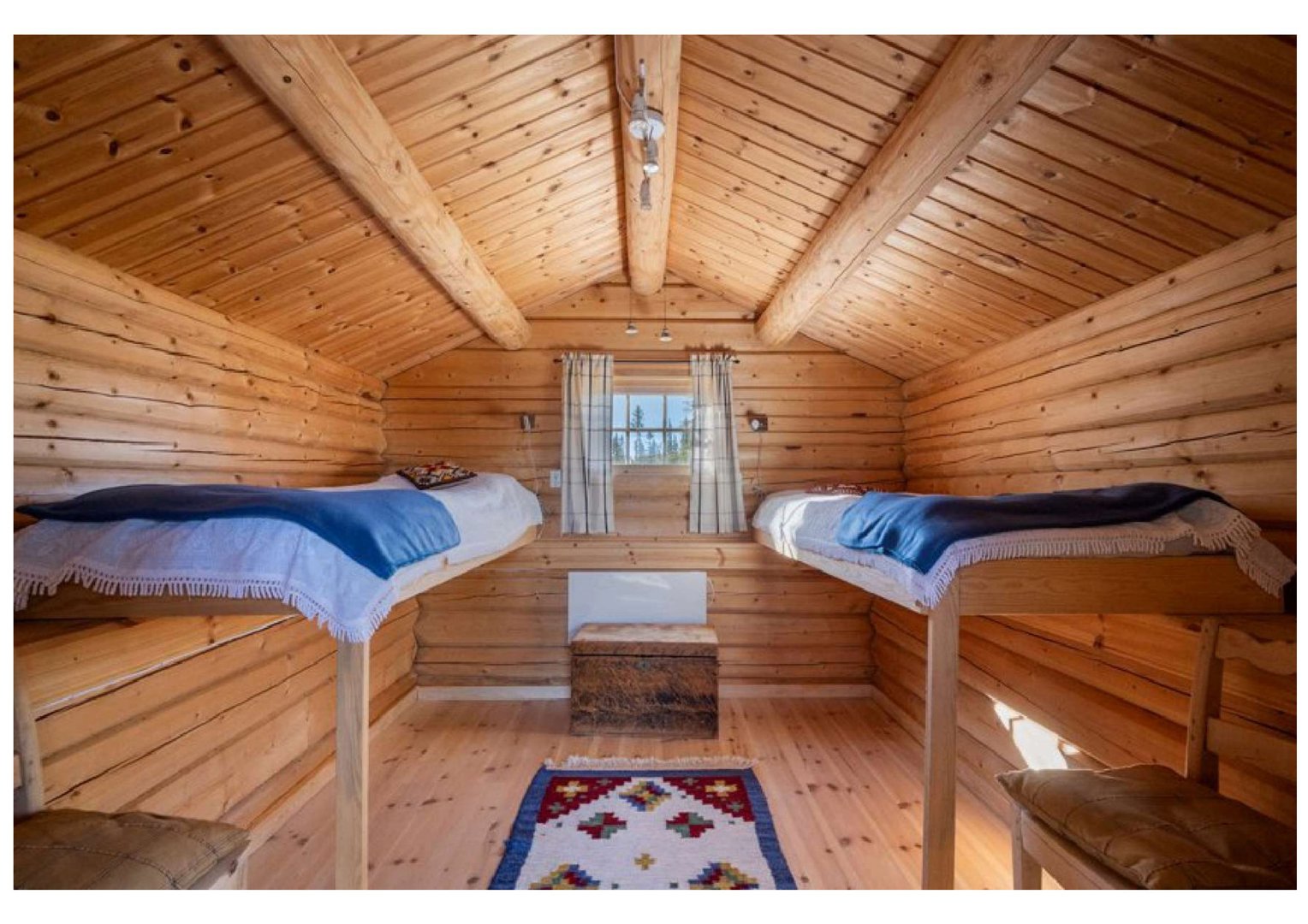 Fotografi av en innredet hytte eller soverom med senger, gulv og tak i tre.